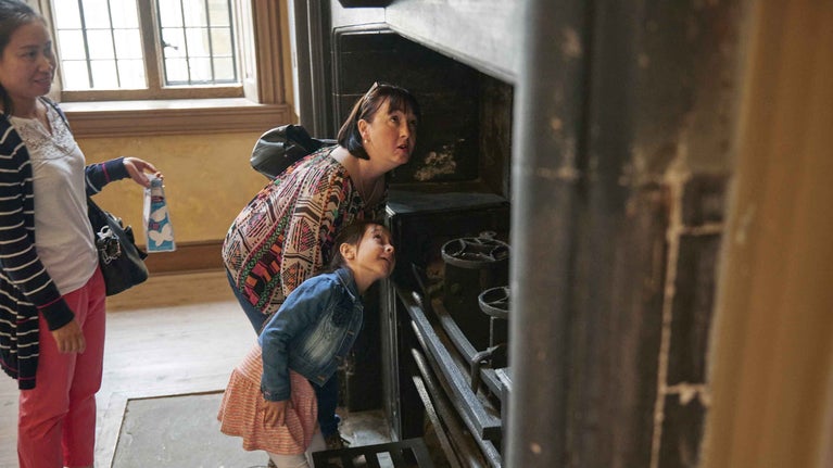 Two adults and a child peek up into a chimney above a stove inside the house at Dyrham Park, Gloucestershire